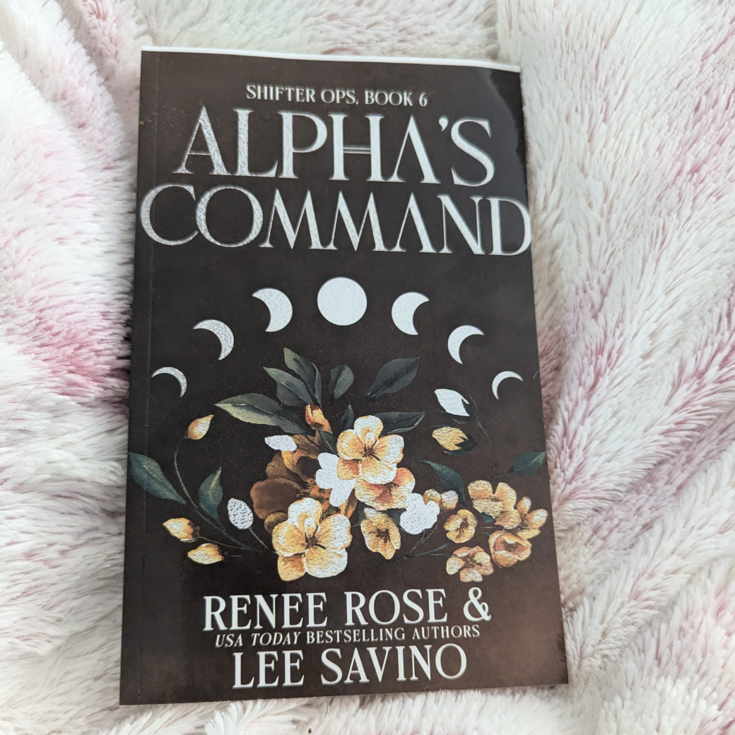 Photo of the front alternate cover of the "Alpha's Command" paperback. The cover features yellow flowers and the moon cycle. 